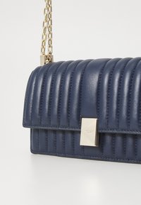 Navy leather handbag with quilted design, gold metal chain strap, and a rectangular clasp featuring a subtle logo accent.