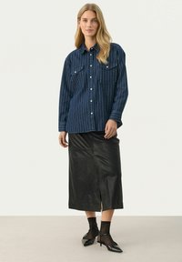 Denim shirt with white vertical stripes, two chest pockets, and button closure, paired with a black leather midi skirt and pointed heels.