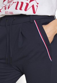 Pantalons de jogging navy en tissu doux, avec une taille élastique à cordon de serrage et des bandes latérales aux accents rouge, blanc et bleu.
