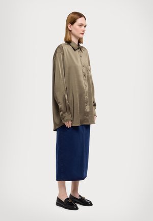 Olivengrønn satengskjorte med knapper og lomme, kombinert med en mørkeblå denimskjørt som rekker til kneet og svarte loafers med gullakenter.