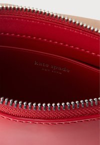 Piros bőrtáska belseje ezüst cipzárfogakkal és a "kate spade NEW YORK" logóval, mely belül bevésett.