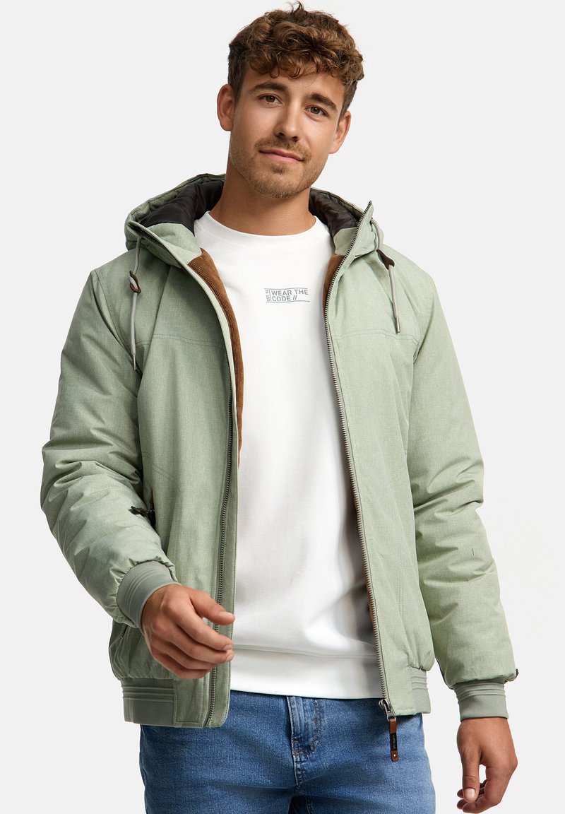 Light green bomber jacket with a hood, featuring a zip front, elastic cuffs, and subtle brown accents. Worn over a white shirt.