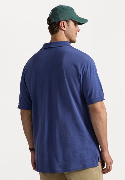 Βραχίονας πόλο κοντομάνικο σε σκούρο μπλε ύφασμα, με πλάκα δύο κουμπιών, κλασικό γιακά και πλάγιες σχισμές στο τελείωμα.