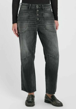 Zwart vervaagde spijkerbroek met grote voorzakken en knoopsluiting, gedragen met zwarte loafers en een zwart top met lange mouwen.