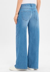 Weite Jeans aus hellblauem Denim, mit einem mittelhohen Bund und zwei hinteren Taschen mit Steppdetails. Strukturierte Stoffoberfläche.