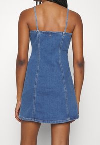 Robe en denim avec des bretelles fines, corsage ajusté et jupe évasée. Tissu bleu avec une texture lisse et des détails de couture visibles.