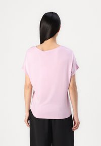Top rosa a maniche corte con vestibilità ampia e scollatura rotonda. Realizzato in un tessuto morbido con una texture liscia. L'orlo è leggermente curvato.