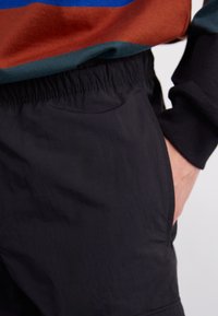 Zwarte, lichtgewicht shorts met een elastische tailleband en zijzakken, gecombineerd met een meerkleurige, gestructureerde longsleeve shirt.