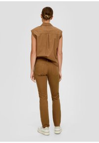 Chemise en coton marron à manches courtes et plis au dos, associée à un pantalon marron ajusté. Stylée avec des baskets blanches.