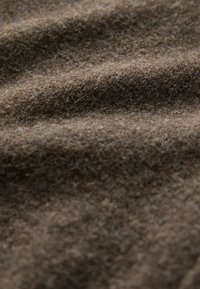 Gros plan sur un tissu en laine brune douce et texturée montrant sa surface duveteuse et ses fibres naturelles dans de doux plis.