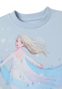 Lichtblauwe sweatshirt met een gedrukt illustratie van een personage met lang blond haar, fonkels en vloeiende ijskoude blauwe accenten.