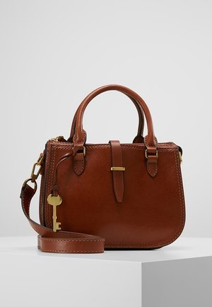 Braune Lederhandtasche mit zwei Griffen, einem abnehmbaren Schulterriemen und einem dekorativen goldfarbenen Schlüsselanhänger auf einem weißen Sockel.