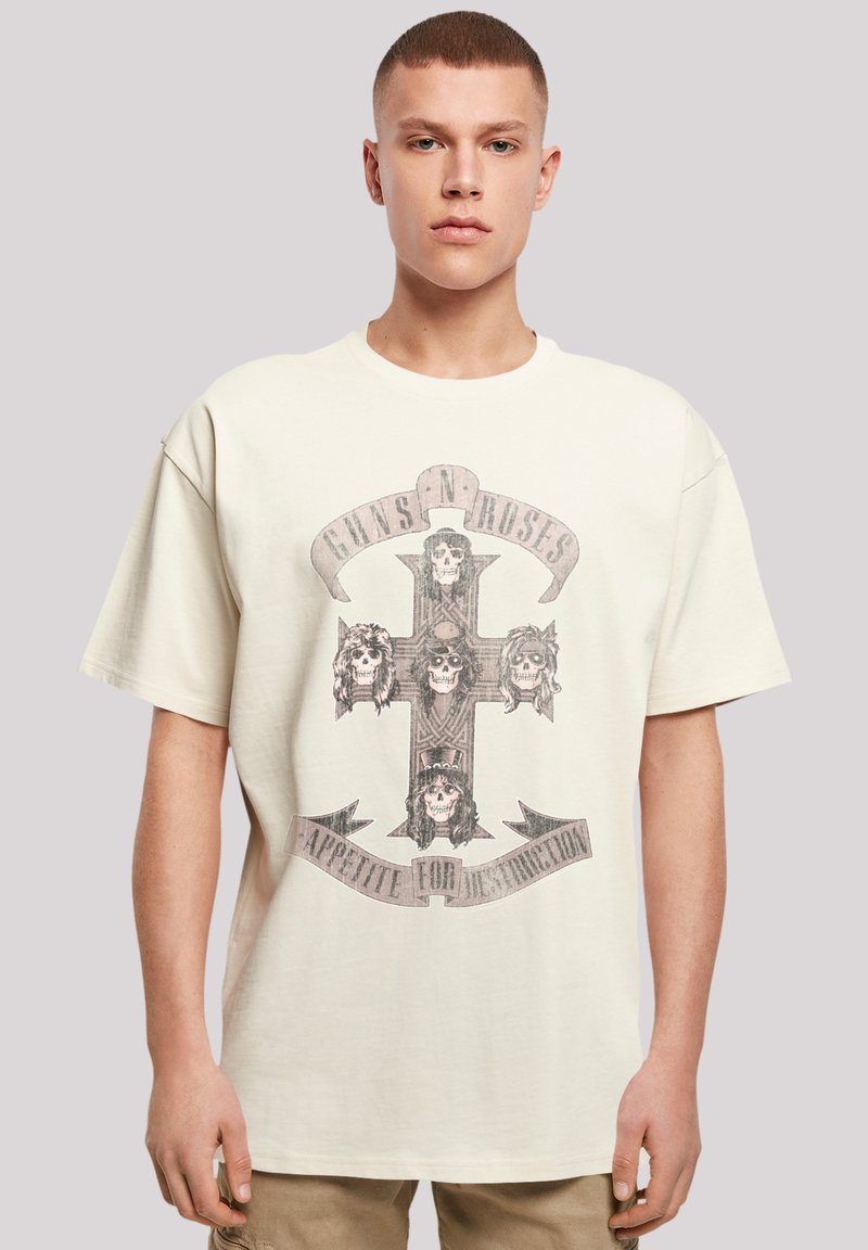 Light beige oversized T-shirt featuring a graphic design of a cross with skulls and "Guns N' Roses" text, made from cotton with a soft texture.