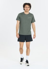 Camiseta deportiva de manga corta en color verde, hecha de tejido ligero, combinada con pantalones cortos negros. Presenta un cuello redondo y un detalle de logo mínimo.