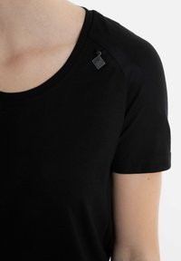 Zwarte t-shirt met korte mouwen en ronde hals, gemaakt van een zachte stof, met een klein label op de schouder en een gladde textuur.