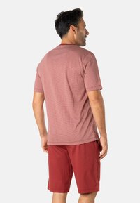 Chemise à manches courtes rouge à motifs avec un col rond, associée à un short rouge. La chemise présente un design texturé et une coupe décontractée.