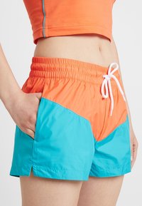 Barevné plavky s designem v oranžové a tyrkysové barvě, elastický pas, šňůrka na stažení a postranní kapsy. Hladká, lehká tkanina.
