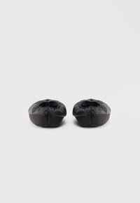Chaussures noires rembourrées avec une forme arrondie et des ouvertures élastiques, dotées d'une texture lisse et de semelles en caoutchouc plates.