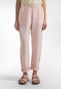 Lichtroze linnen broek met een elastische tailleband met trekkoord, taps toelopende pijpen en opgerolde boorden, gecombineerd met lichtroze sandalen met een gesp.
