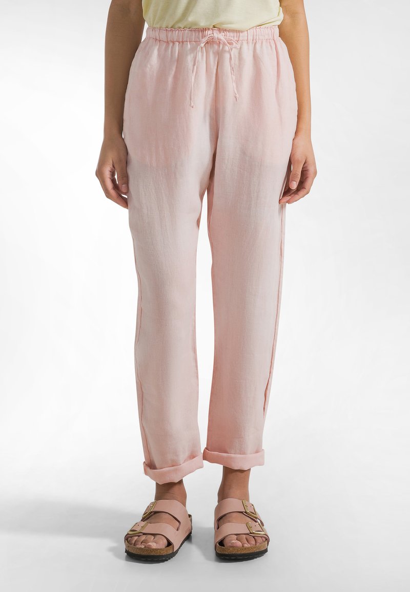 Lichtroze linnen broek met een elastische tailleband met trekkoord, taps toelopende pijpen en opgerolde boorden, gecombineerd met lichtroze sandalen met een gesp.