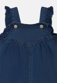 Abito in denim con spalline arricciate, corpino arricciato, colore blu scuro e bottoni in metallo per una chiusura sicura. Texture morbida con dettagli di cucitura.