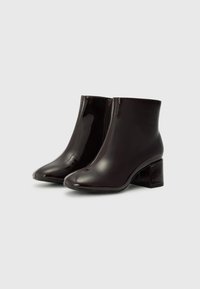 Botas de tobillo burdeos con un acabado brillante, punta afilada y tacón cuadrado, con cremallera lateral y textura suave.