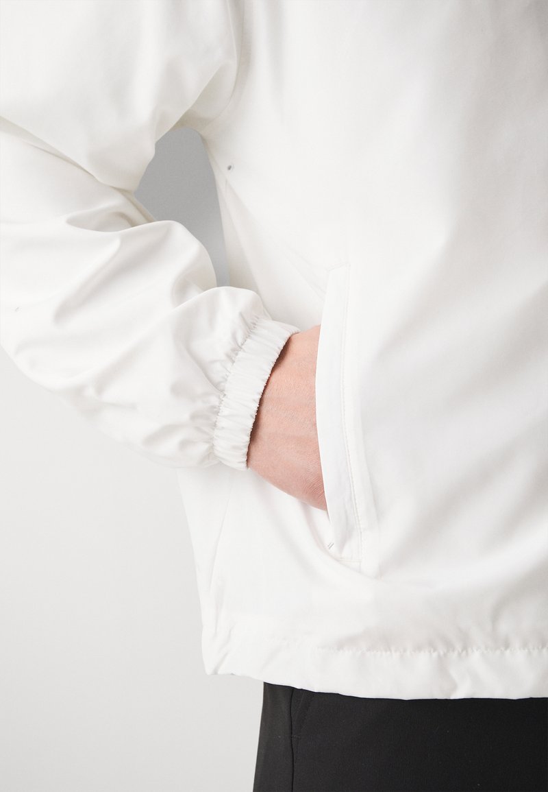 Weißer Windbreaker mit elastischen Bündchen und einer Seitentasche. Glatte Stofftextur und lockere Passform, mit einem dezenten Glanz.