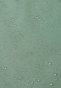 Gros plan sur un tissu vert avec de nombreuses gouttes d'eau claires perlées à la surface, montrant une texture résistante à l'eau.