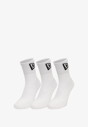 Weiße Knöchelsocken mit geripptem Muster und einem schwarzen Logo am Bund. Drei Paar nebeneinander präsentiert.