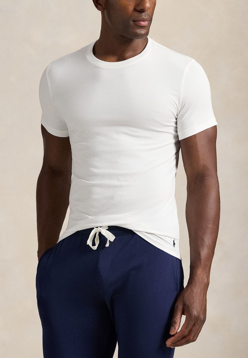 T-shirt blanc en coton avec col rond et manches courtes, associé à un pantalon bleu marine à cordon de serrage, avec un petit logo sur le pantalon.