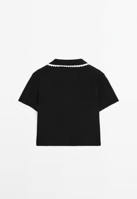 Polo noir en maille avec manches courtes et bordure festonnée blanche le long du col et des manches. Tissu texturé, forme structurée.