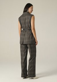 Completo a quadri grigio con blazer senza maniche e pantaloni a gamba larga. Tessuto testurizzato, motivo a quadri sottile e accenti più chiari a contrasto.