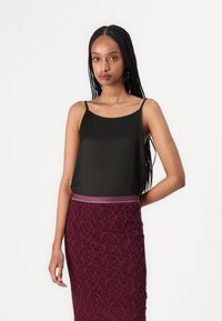 Schwarzes Satin-Camisole mit dünnen Trägern, kombiniert mit einem burgunderfarbenen Spitzen-Midirock, der ein strukturiertes Muster und ein kontrastierendes Taillenband aufweist.