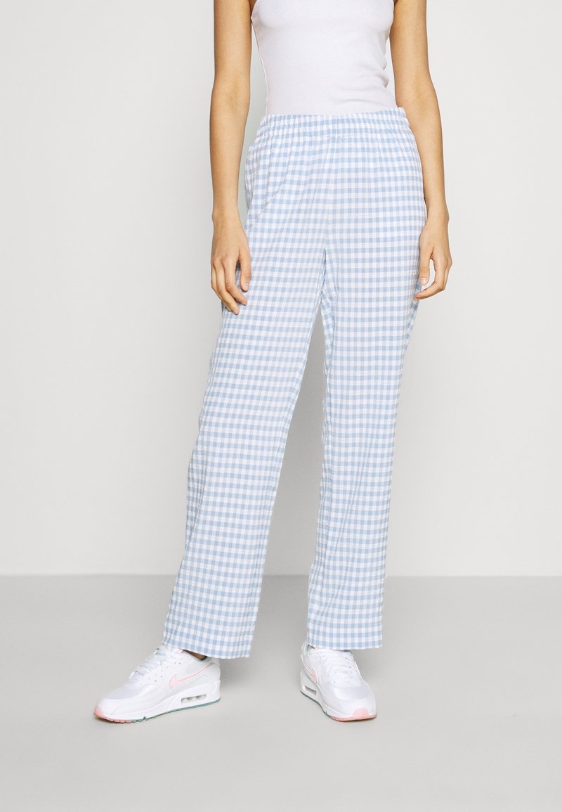 Ljusblå och vit rutig byxor med elastisk midja och bred benvidd, i kombination med vita sneakers. Slät tygtextur.