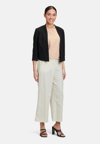 Zwarte cropped jas, beige top, lichtbeige broek, zwarte sandalen met bandjes. Gladde stof en getailleerde pasvorm met een ontspannen silhouet.