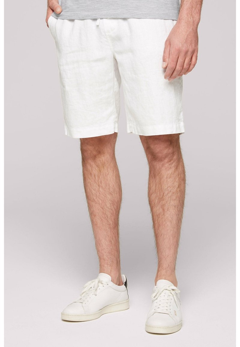Shorts en lin blanc à coupe décontractée, avec une taille à cordon et un ourlet retroussé, associés à des baskets blanches.