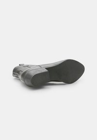 Botín de cuero negro hasta el tobillo con punta redonda y tacón bajo; presenta una superficie lisa y acentos mínimos para un diseño elegante.