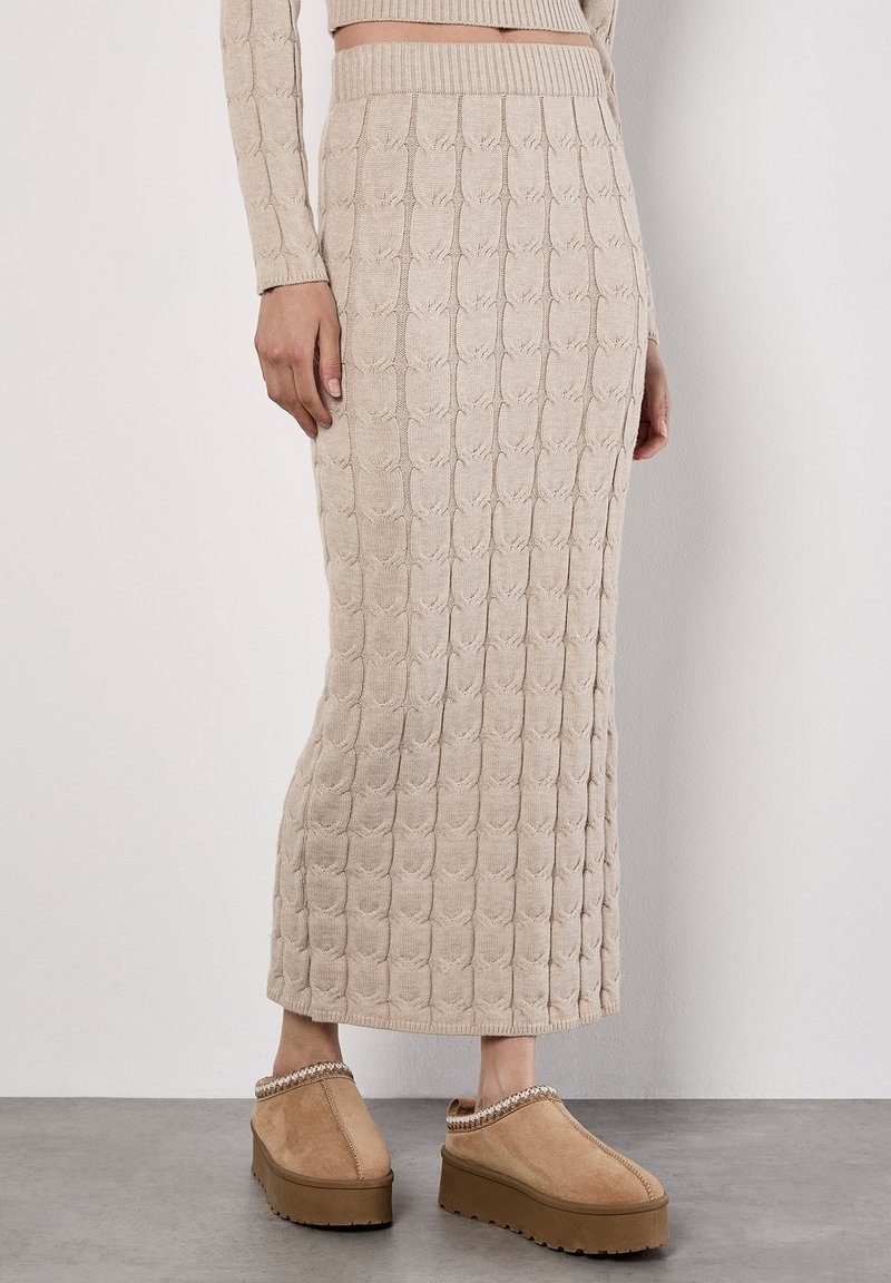 Beige gestrickter Midirock mit strukturiertem Muster, geripptem Bund und seitlichem Schlitz. Kombiniert mit hellbraunen Slippern.