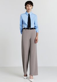 Hellblaues langärmliges Hemd, schwarze Krawatte, graue weite Hose, schwarzer Gürtel, weiße spitze Absätze. Minimalistisches Design mit glatter Textur.