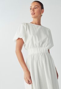 Biała sukienka z krótkimi bufkowymi rękawami, elastyczną talią, zwiewnym dołem i gładką fakturą; minimalistyczny design z okrągłym dekoltem.