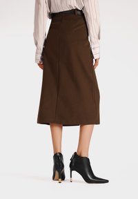 Gonna A-line marrone realizzata in tessuto testurizzato, arriva a metà polpaccio. Abbinata a stivali neri in pelle fino alla caviglia con punta affusolata e tacco metallico.