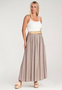 Maxirock aus leicht beigem Stoff mit gerafftem Design, kombiniert mit einem weißen, taillierten Oberteil und einem hellbraunen Gürtel. Plateausandalen runden den Look ab.