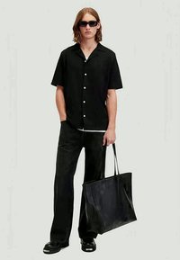 Camicetta nera a maniche corte con bottoni, abbinata a pantaloni neri a gamba larga e una borsa tote nera, caratterizzata da una texture liscia e un design minimalista.