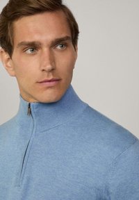 Jasnoniebieski sweter z dzianiny z wysokim kołnierzem na zamek, teksturowana tkanina i dopasowany krój, prezentujący gładkie wykończenie i subtelne detale.