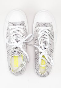 Zapatillas de lona blanca con patrón de rayas negras, punta redonda y cordones blancos. Forro suave con un acento amarillo en el interior. Suela de goma.