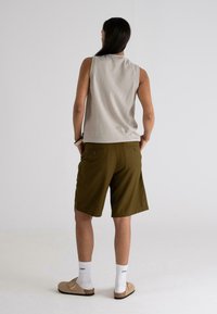 Beige ujjatlan felső, laza szabással, olívazöld rövidnadrág, barna slip-on cipők és fehér bokazokni. Egyszerű dizájn és semleges színek.