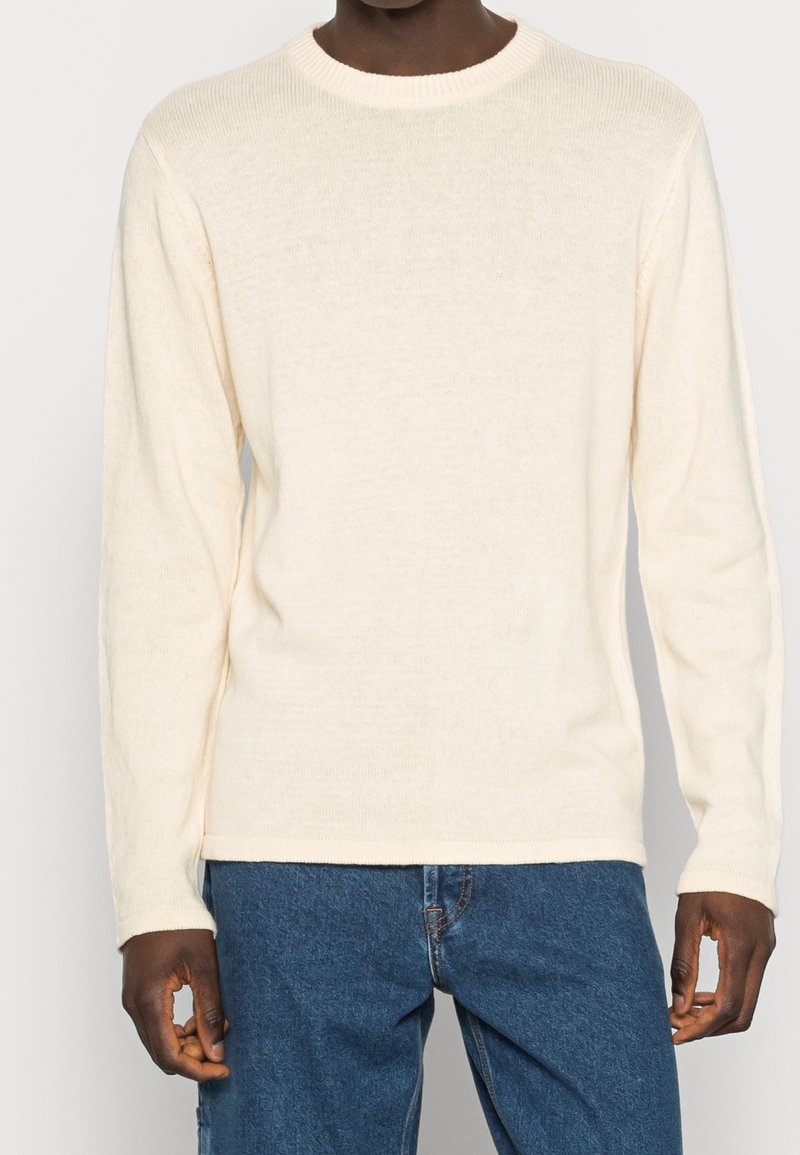 Maglione a maniche lunghe color crema con scollatura rotonda a coste. Realizzato in un morbido tessuto testurizzato. Abbinato a jeans in denim blu.