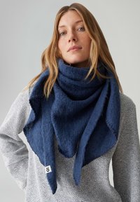 Marineblauwe sjaal van gestructureerde stof, driehoekige vorm met gedrapeerde uiteinden, gedragen over een lichtgrijze gebreide trui. Voorzien van merketiket.