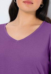 Fialové tričko s výstřihem do V z hladké bavlny, s krátkými rukávy a jemným leskem. Výstřih má čisté švy.