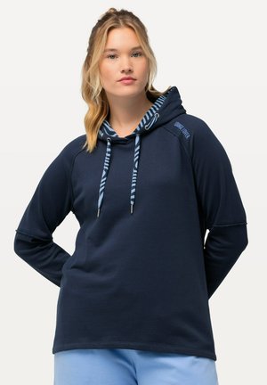 Haut à capuche bleu marine avec une doublure à motif, cordon de serrage et poignets côtelés. Matière douce, coupe décontractée, accentué par le texte « Lounge Lover ». 